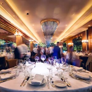 Upscale restaurant dining room with white tablecloths, crystal glassware, and motion-blurred waiters in background.