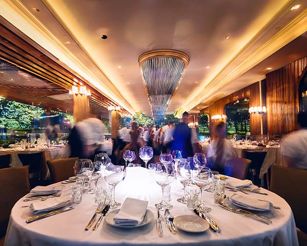 Upscale restaurant dining room with white tablecloths, crystal glassware, and motion-blurred waiters in background.